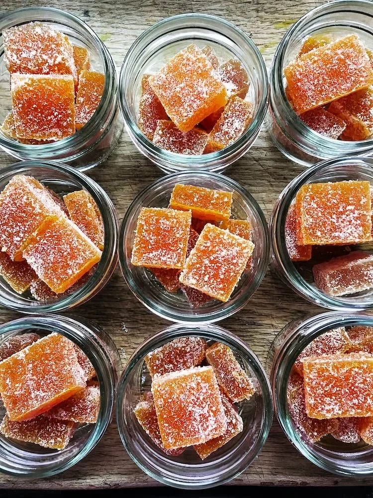 Colorful homemade fruit jellies neatly arranged in glass jars, showcasing their vibrant orange hue and sugary coating, perfect for dessert or snacking.