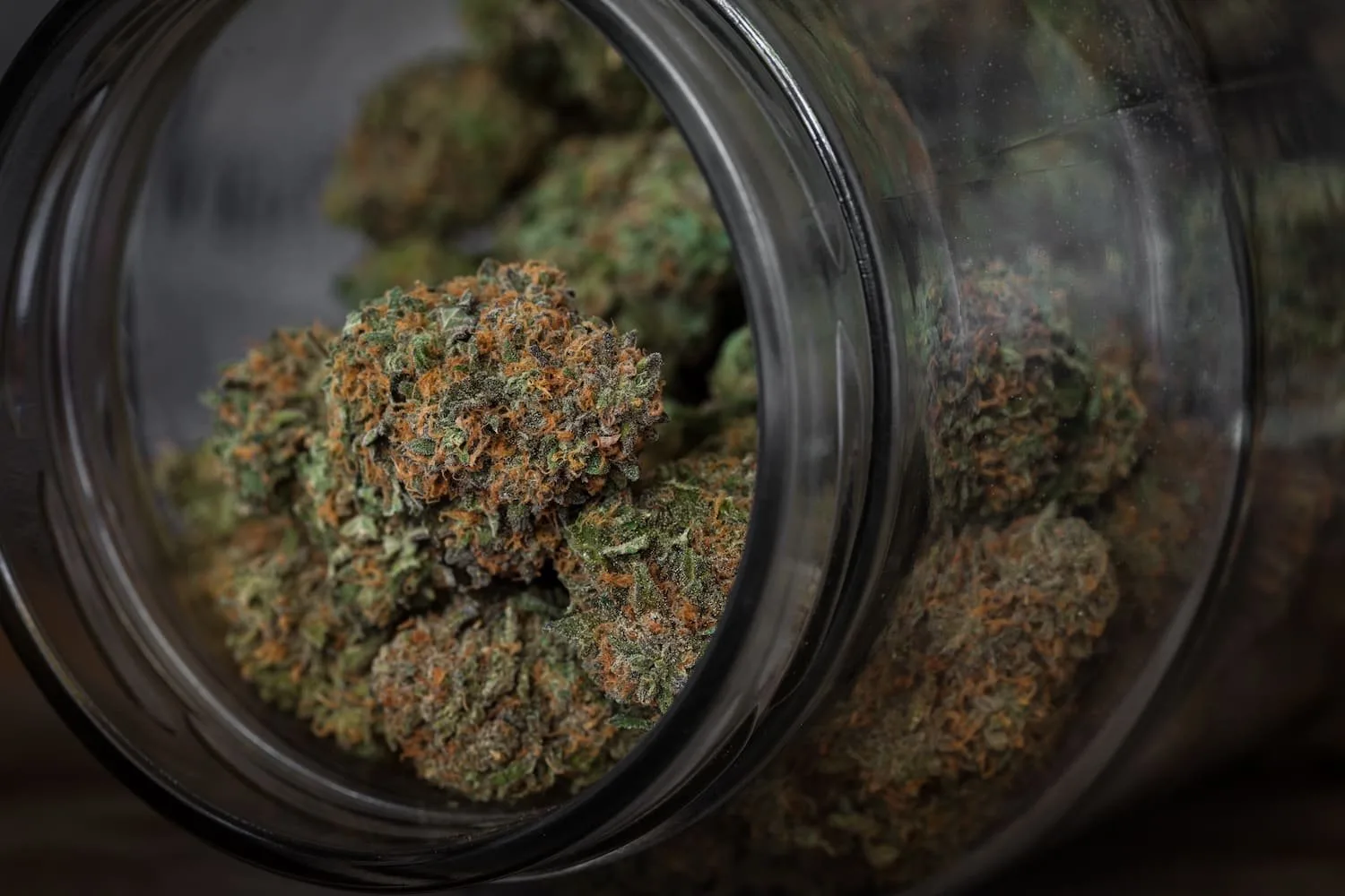Close-up of cannabis buds in a glass jar, showcasing the vibrant green and orange hues, highlighting the texture and quality of the marijuana strain.