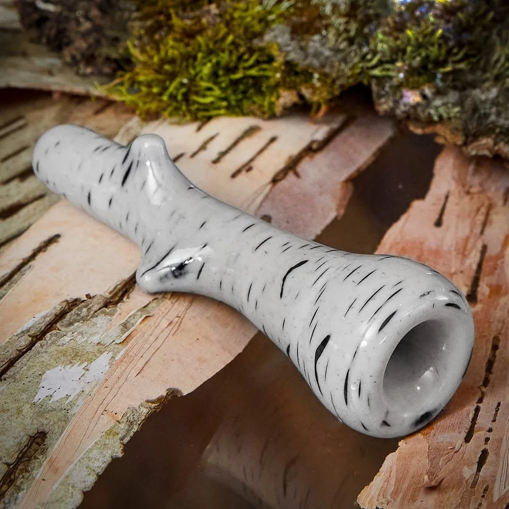 Handcrafted white and black marble smoking pipe resting on natural birch bark, featuring a unique branch-like design. Ideal for collectors and smoking enthusiasts.