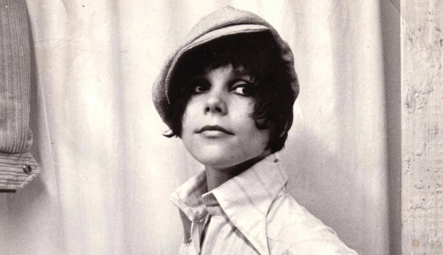 Black and white portrait of a young person wearing a cap and collared shirt, gazing slightly upward with a thoughtful expression