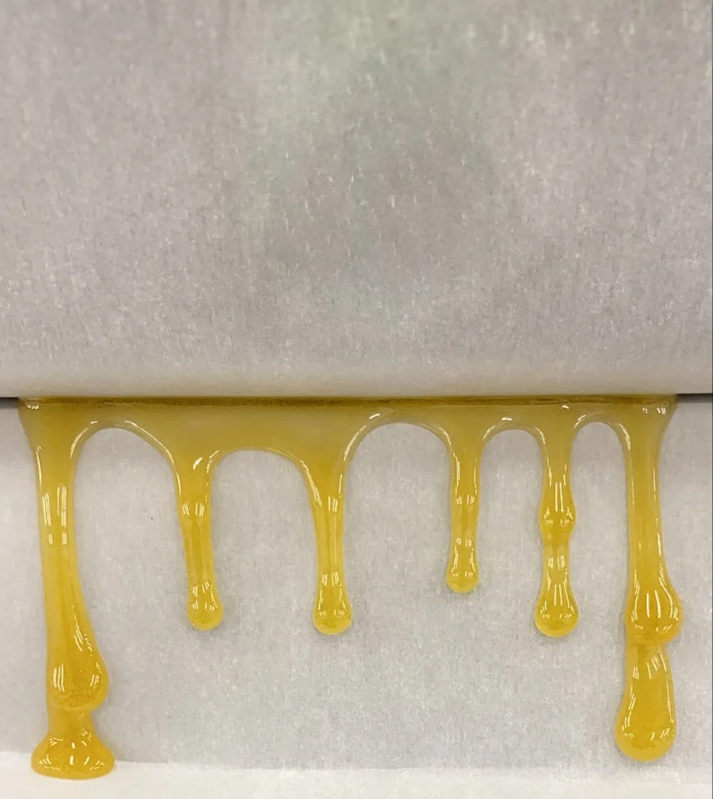 Golden honey dripping onto parchment paper, showcasing its thick and viscous texture, highlighting the natural sweetness and rich color.
