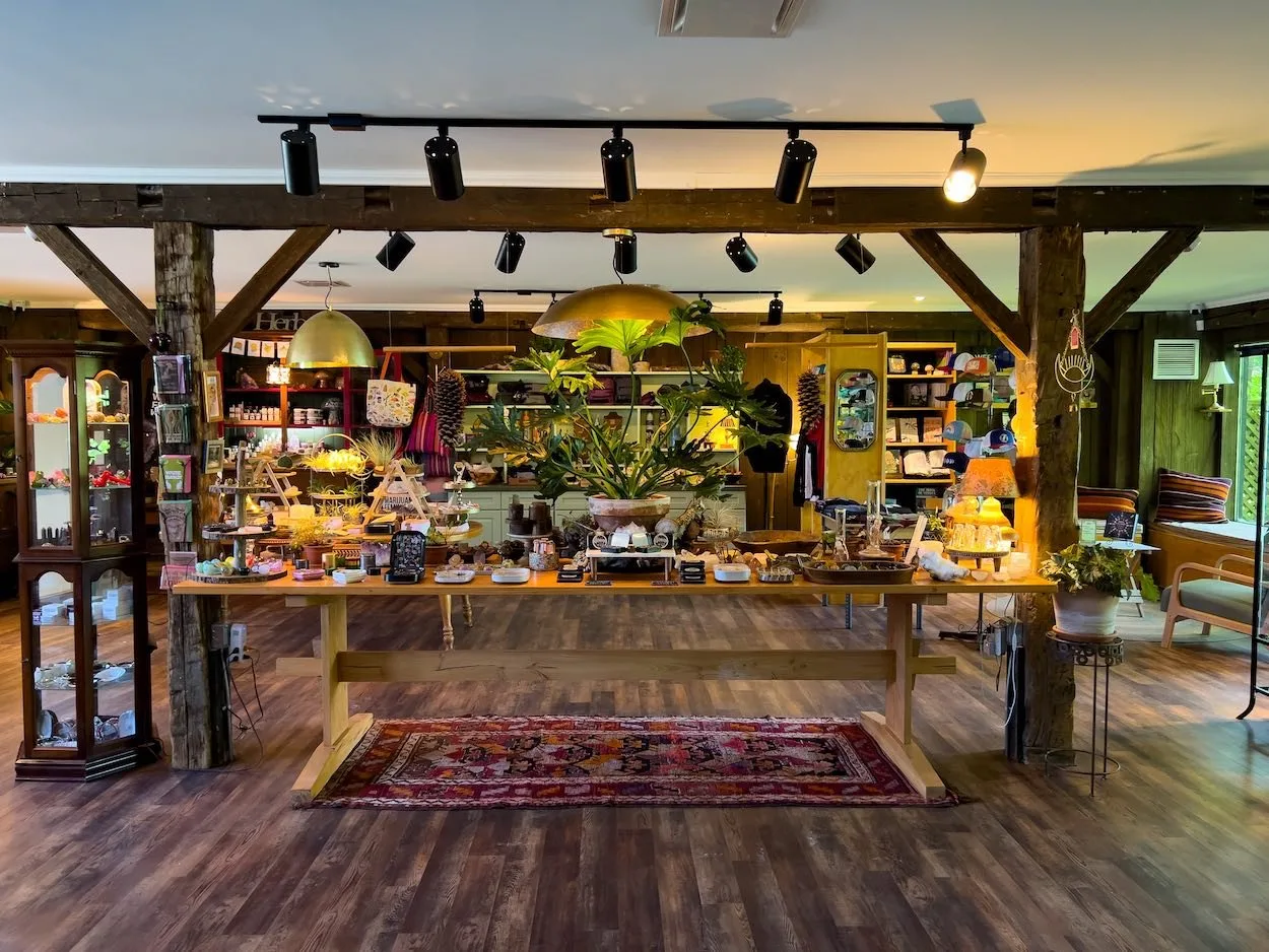 Rustic boutique interior with wooden beams, shelves of colorful products, a long wooden table displaying plants, crafts, and decor under warm lighting